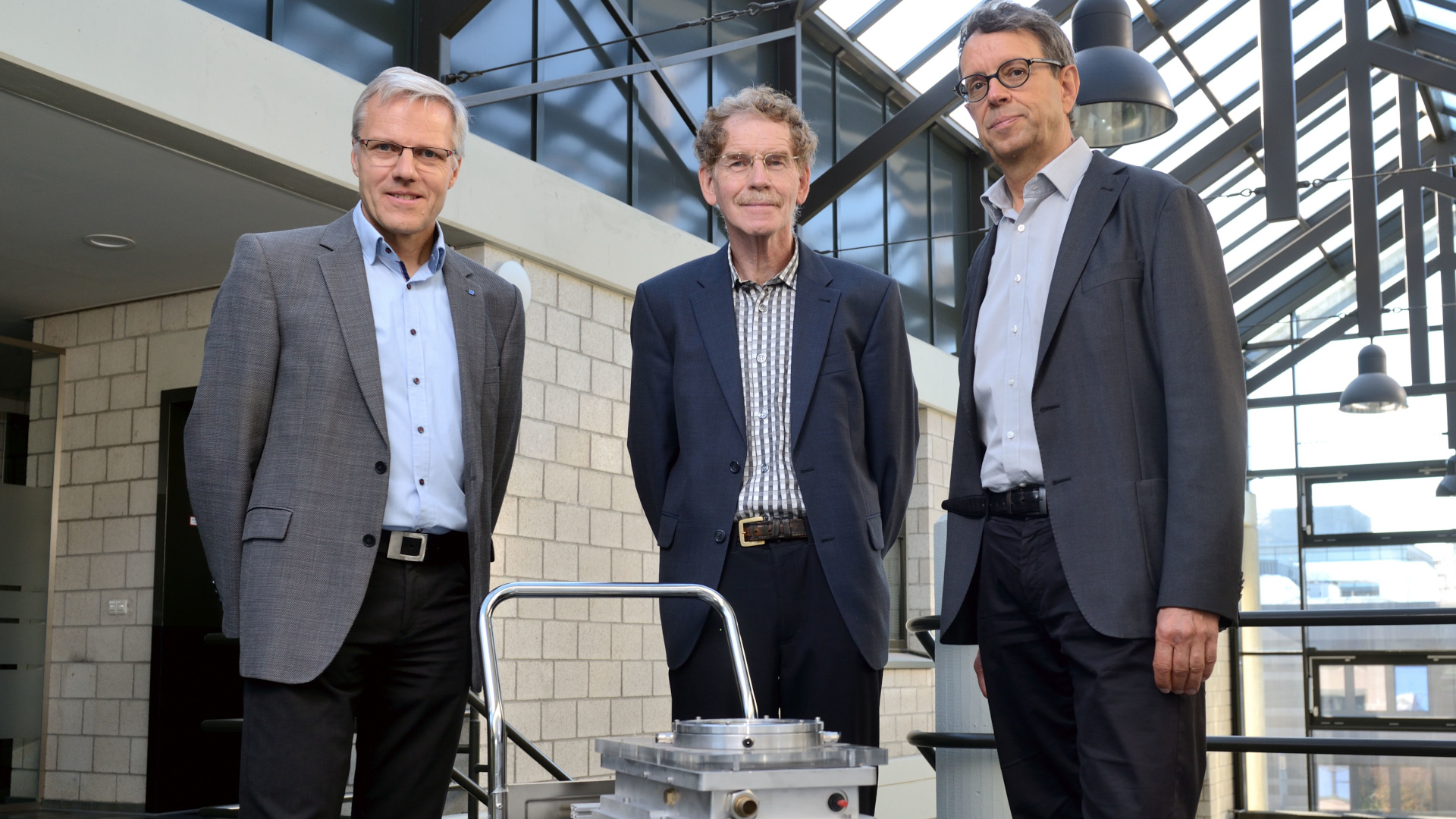 The inventors of the process, Wilhelm Meiners, Kurt Wissenbach and Andres Gasser, stand in front of a small transport trolley with the first LPBF machine.